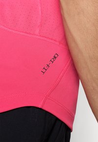 Camisa atlética ajustada en un vibrante color rosa con una textura suave, que presenta un logotipo negro y perforaciones transpirables cerca del hombro.