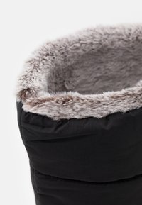 Zbliżenie górnej części czarnego zimowego buta z miękkim, szaro-brązowym futrem syntetycznym w okolicy otworu.