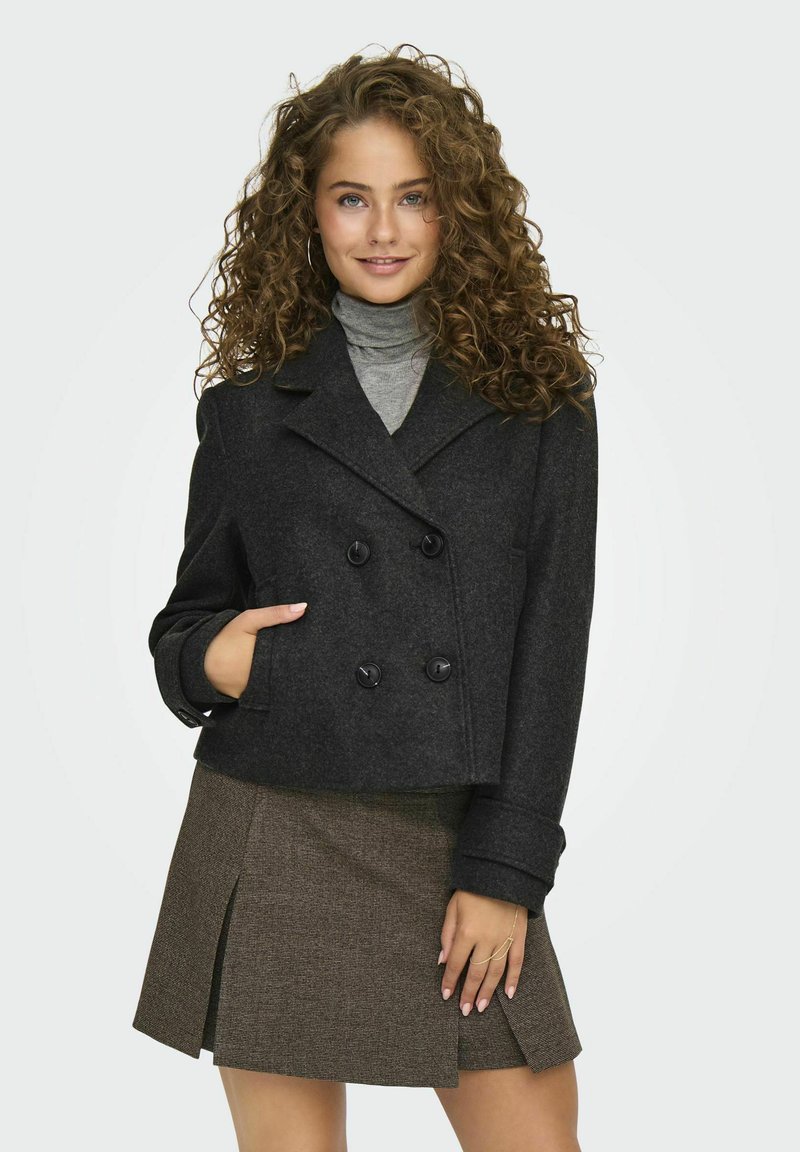 Črn, dvoredni skrajšan volnen plašč z črnimi gumbi in žepom. Nosi se preko sivega turtleneck puloverja in teksturirane rjave krila.