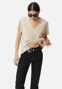 T-shirt beige a scollo a V realizzato in materiale morbido, con maniche corte, vestibilità rilassata, abbinato a pantaloni neri a vita alta e una cintura.