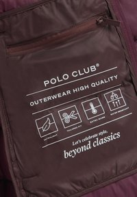 Wewnątrz kieszeni ciemnofioletowej kurtki z etykietą "Polo Club", podkreślającą ultralekkie, dopasowane kroje, dodatkowe ocieplenie i wodoodporność.