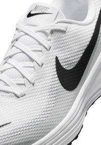 Zapatilla deportiva blanca con parte superior texturizada, logo de Nike en negro y cordones blancos planos. Presenta una suela acolchada y elementos de diseño ligeros.