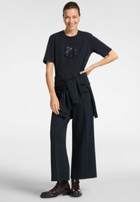 T-shirt marine avec un graphique en sequins, associé à un pantalon marine ample et des bottines chelsea marron foncé. Pull noué à la taille.