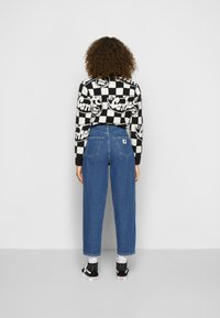 Černo-bíle kostkovaný svetr s nápisem, džíny s vysokým pasem z modrého denim, a černé tenisky s bílými detaily a vzorovanými ponožkami.