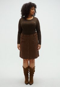 Cămașă maro cu mâneci lungi și imprimeu de leopard, asortată cu o fustă maro din catifea cu nasturi în față. Cizme maro până la genunchi.