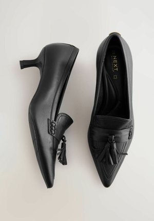 Pantofi negri din piele cu toc înalt, cu un design cu vârf ascuțit, având un accent cu ciucure împletit și un finisaj neted. Toc plat pentru stabilitate.