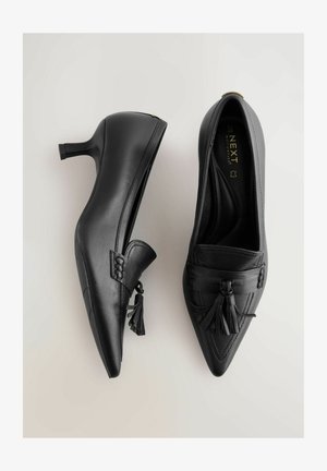 Zwarte leren hoge hakken met een puntige neus, voorzien van een geweven kwastaccent en een gladde afwerking. Platte hak voor stabiliteit.