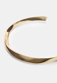 Traka za glavu od metalnog materijala zlatne boje s glatkim, zakrivljenim dizajnom. Površina je sjajna s blagim valovitim uzorkom i suženim krajem.
