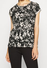 Černobílé květinové tričko s krátkým rukávem, kulatým výstřihem a volným střihem, vyrobené z měkké, texturované látky.
