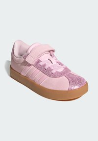 Pink sneakers with a velcro strap, featuring sparkly accents, suede texture, and a gum rubber sole. Three stripes logo on side.