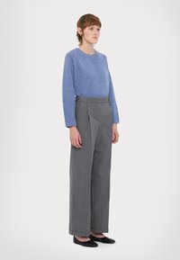 Maglione blu lavorato a maglia con maniche lunghe, abbinato a pantaloni larghi a coste grigi a vita alta. Completano il look delle semplici ballerine nere.