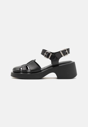 Zwarte leren platform sandalen met open teen en meerdere kruisbanden, voorzien van een enkelband met twee metalen gespen en een chunky hak.