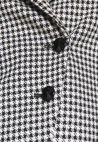 Tissu à motif pied-de-poule en noir et blanc avec deux boutons noirs visibles cousus en ligne verticale.
