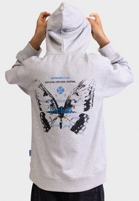 Felpa grigia con cappuccio caratterizzata da una grafica di una farfalla nera sul retro con testo blu. Tessuto morbido, vestibilità rilassata e polsini a coste.