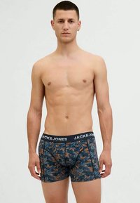 Boxers para hombres con un diseño estampado de hojas en verde y naranja sobre un fondo azul oscuro, con una cintura negra que muestra el nombre de la marca.