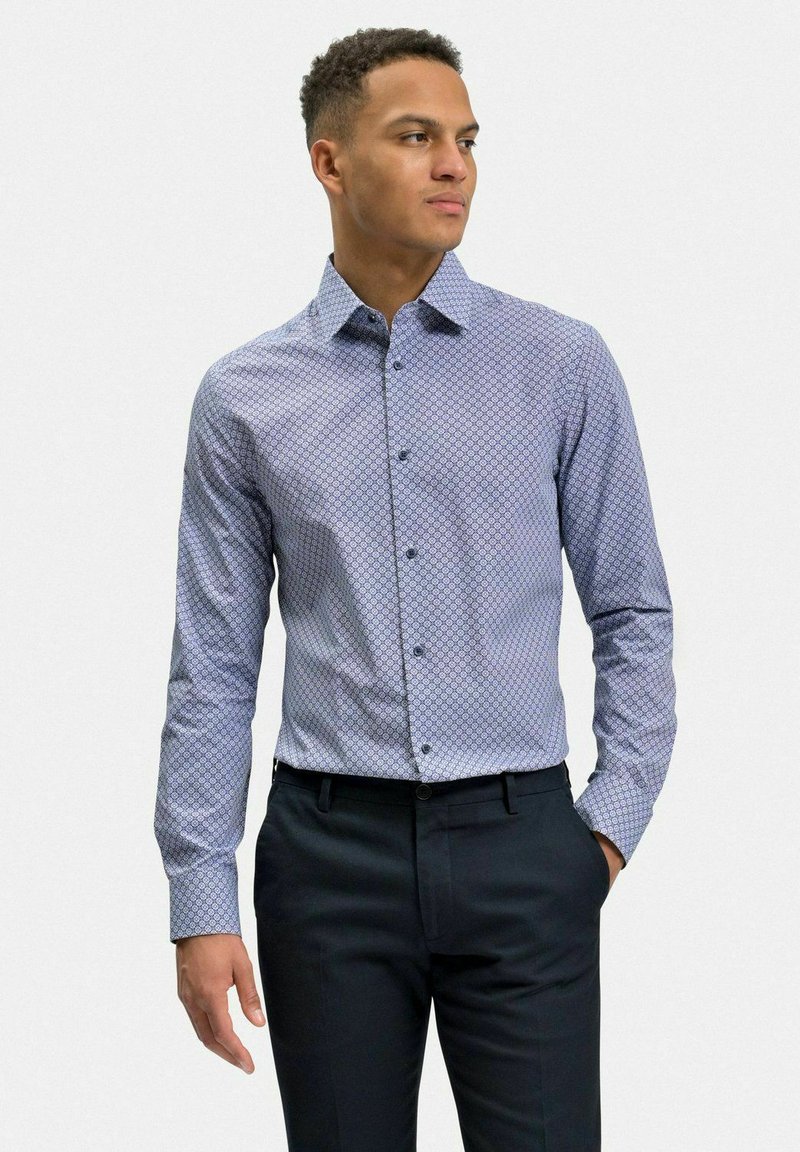 Blå skjorta med knappar och ett geometriskt mönster, långa ärmar och spridd krage. Bärs med mörka byxor. Slät textur.