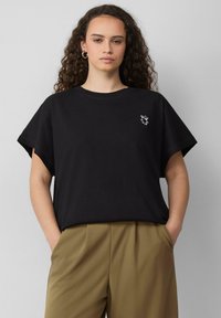 T-shirt en coton noir à manches courtes, avec un petit graphique de verre à boisson blanc sur la poitrine gauche. Coupe décontractée et texture douce.