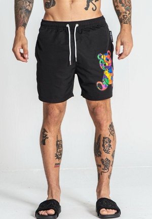 Schwarze Badeshorts mit einem bunten Bärenmotiv auf dem rechten Bein. Verfügt über einen elastischen Bund und eine weiße Schnürung.