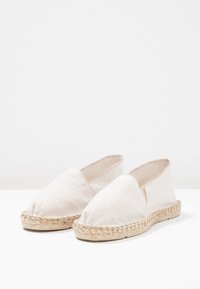 Beige canvas espadrilles with a woven jute sole, rounded toe, and elastic sides for easy slip-on. Minimalistic design with no visible logos.
