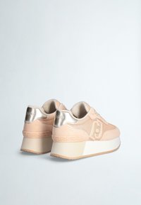Sneakers piattaforma eleganti in suede rosa blush con dettagli metallici oro, caratterizzati da un tallone testurizzato e un motivo intricato lungo la suola.
