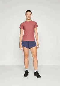 Atletski komplet, ki vključuje kratkosleeveno roza majico in temno modre kratke hlače. Vsebuje črne športne copate in bele gležnjarje. Enostaven dizajn.