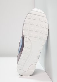 Grå sneaker sula med en strukturerad vit gummiyttersula, med blå detaljer längs sidan och ett slätt grått ovanside-material.