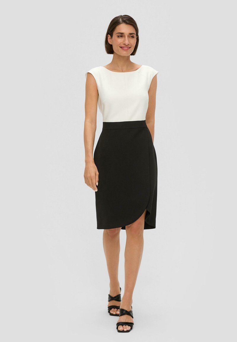 Robe noire portefeuille avec un buste blanc ajusté, des manches courtes et une fente sur le côté. Texture lisse et design minimaliste souligné par une silhouette élégante.