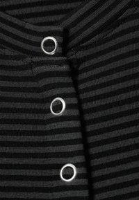 Tissu rayé noir et gris avec trois boutons circulaires argentés au niveau de l'encolure. La texture semble lisse et extensible.