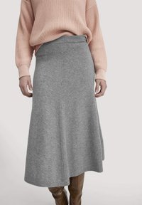 Grauer, gestrickter A-Linie-Rock aus einem weichen Stoff, ausgestattet mit einer hohen Taille und fließender Silhouette, kombiniert mit einem strukturierten rosafarbenen Pullover.