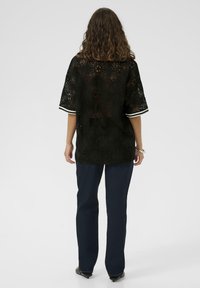 Črna čipkastka bluzica s cvetličnimi vzorci, kratkimi rokavi z belimi črtastimi poudarki, v kombinaciji z temno modrimi naravnim krojem kavbojkami.