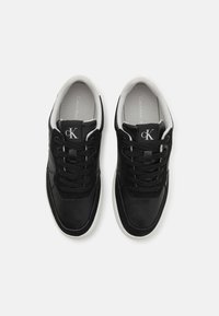 Sneaker in pelle nera con accenti in tessuto, punta rotonda, suola bianca e design con lacci. Presenta un logo sulla linguetta e un morbido rivestimento interno.