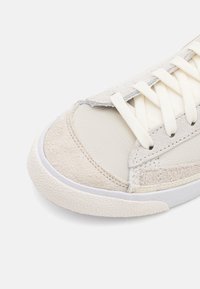 Ljust grå sneaker med en blandning av slät läder och mocka-texturer. Har vita snören och en texturerad gummisula.