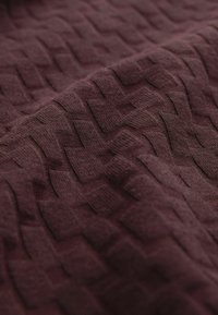 Close-up of textured maroon fabric featuring a woven pattern with raised zigzag shapes, highlighting its intricate design and color.