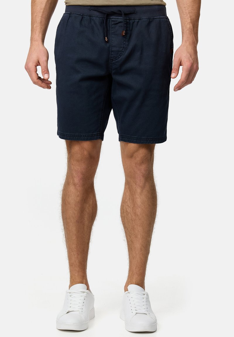 Marineblaue Baumwollshorts mit elastischem Bund, verstellbarem Kordelzug, Seitentaschen und glatter Textur. Getragen mit weißen Turnschuhen.