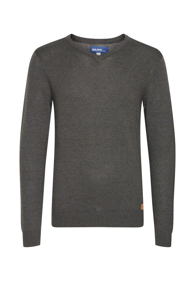 Pull en tricot gris avec un col rond, des poignets et un ourlet côtelés, arborant un petit écusson logo sur le côté inférieur. Texture douce et design classique.