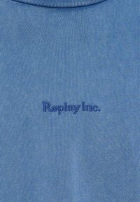 Μπλε ύφασμα με λεπτή ραβδωτή υφή και κεντητό κείμενο "Replay Inc." με κλωστή σε αντίστοιχο μπλε χρώμα, τοποθετημένο στο κέντρο κάτω από μια στρογγυλή λαιμόκοψη.