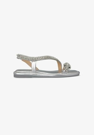 Flat sandals with a metallic silver finish, featuring a bejeweled strap and a decorative rhinestone accent at the toe.