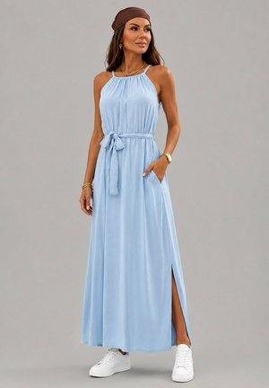 Femme portant une robe maxi sans manches bleu clair avec ceinture à la taille et fente latérale, associée à des baskets blanches et un bandeau marron.