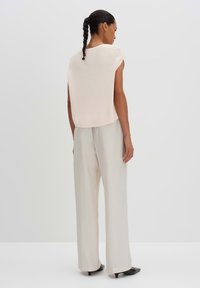 Top a maniche corte di colore beige chiaro in maglia, abbinato a pantaloni grigi chiari a vita alta e scarpe nere a punta. Texture liscia.