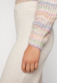 Maglione soffice multicolore a disposizione con righe pastello sulle maniche, abbinato a pantaloni aderenti a coste di un leggero colore beige.