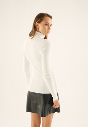 Fitted white ribbed turtleneck sweater with long sleeves, paired with a black leather mini skirt, highlighting texture and design contrast.