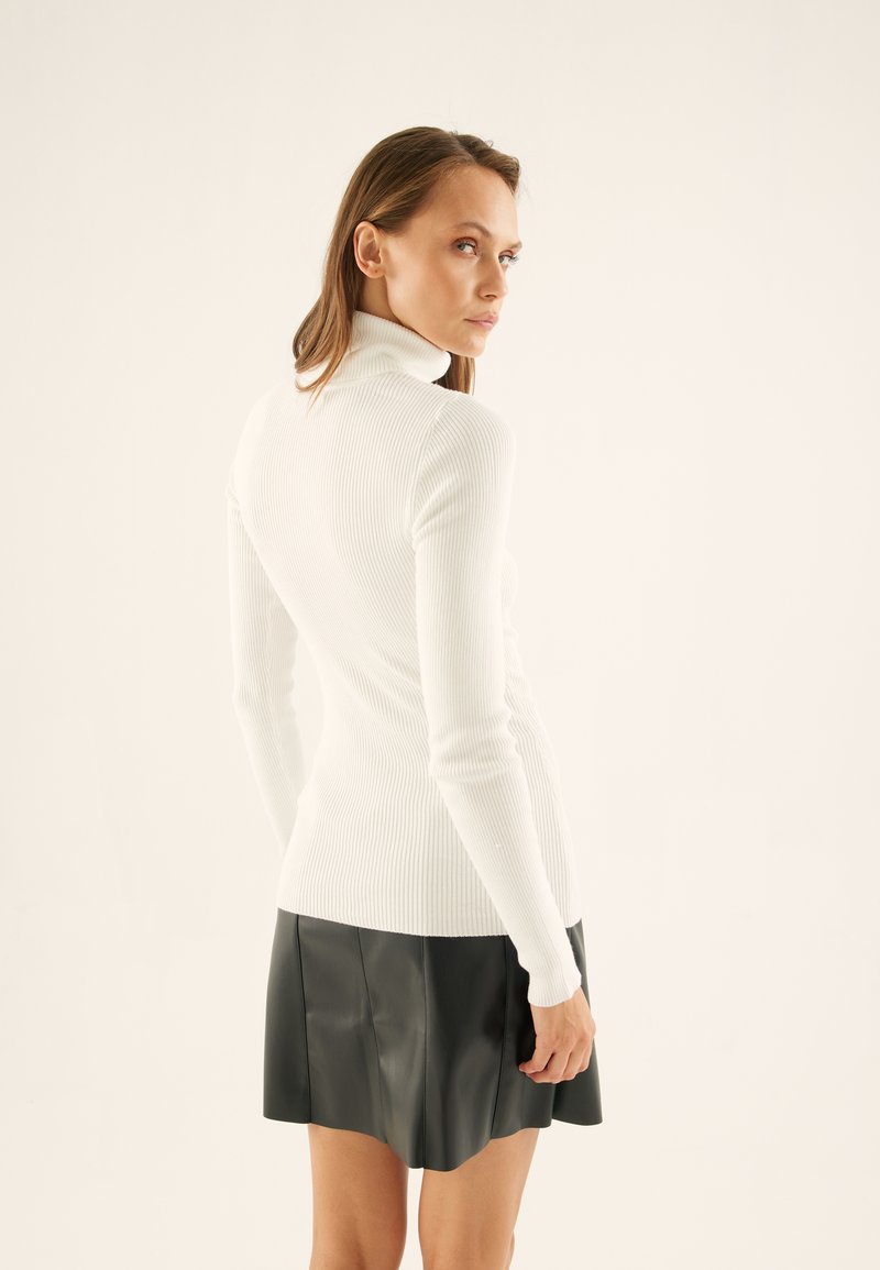 Enganliegende weiße gerippte Rollkragensweatshirt mit langen Ärmeln, kombiniert mit einem schwarzen Leder-Minirock, der Textur und Designkontrast betont.