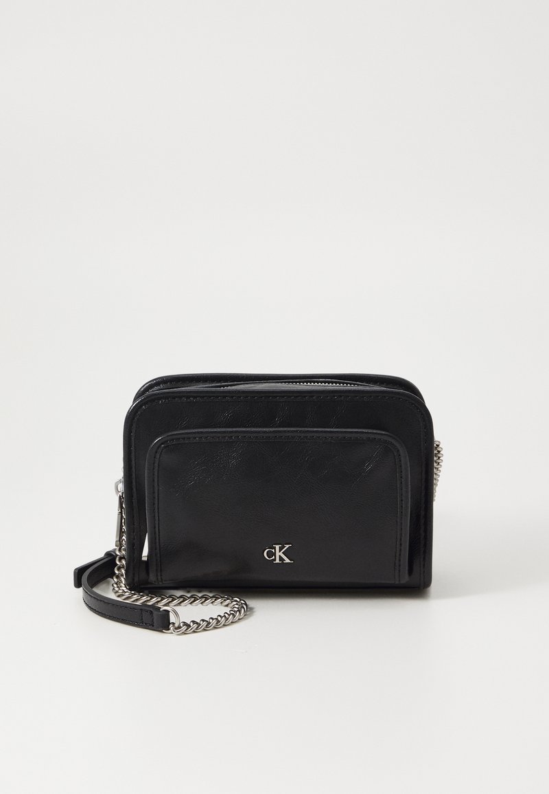 Bolsa de couro preto transpassada com fecho em zíper, bolso frontal e alça de corrente em tom prateado. Inclui um detalhe de logótipo na frente.