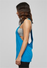 Top blu senza maniche con una vestibilità ampia e design a schiena scoperta. Realizzato in morbido materiale, che rivela una fascia grigia sottostante.