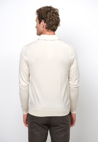 Lichtcrème lange mouwen polo met een kraag, ribgebreide manchetten en onderrand. Soepele textuur en getailleerd silhouet. Donkere broek.