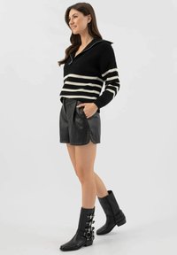 Czarny i biały sweter z paskami, wykonany na drutach, z kołnierzykiem, w połączeniu z wysokimi, czarnymi skórzanymi szortami. Modelka nosi botki za kostkę z klamrami.