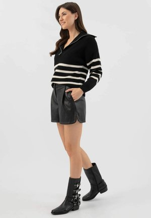 Maglione a righe bianche e nere con colletto, abbinato a pantaloni shorts in pelle nera a vita alta. Il modello indossa stivaletti alla caviglia con fibbie.