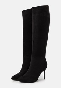Bottes noires montantes au-dessus du genou en daim, avec un bout pointu et un talon haut et fin, présentant une texture lisse sans ornements visibles.