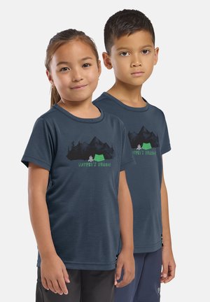 Twee kinderen staan naast elkaar en dragen bijpassende marineblauwe T-shirts met het opschrift "Nature's Nomads" en afbeeldingen van bergen, een tent en een kampvuur.