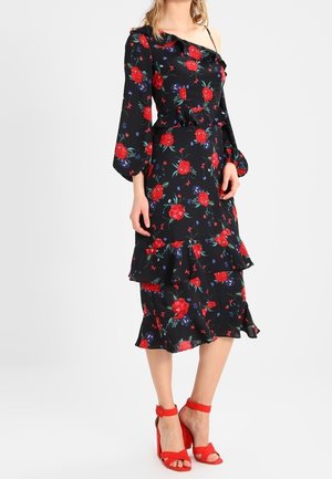 Abito floreale nero con rose rosse, una manica scoperta, orlo arricciato e design a strati. Abbinato a sandali con tacco alti rossi.